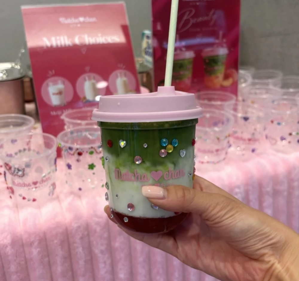 Hand holding a layered Matcha-chan matcha latte with a pink lid at a pop-up