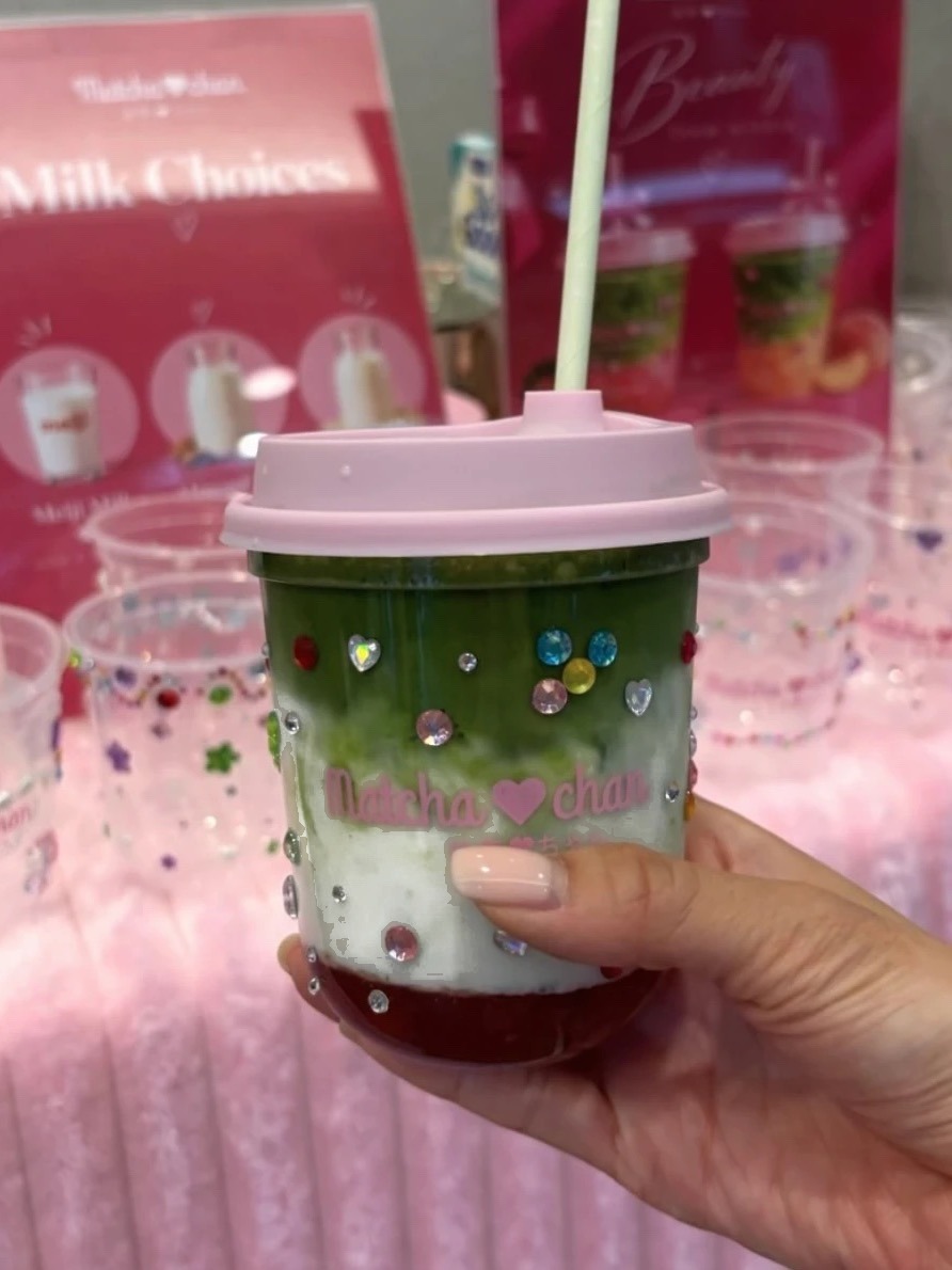 Hand holding a layered Matcha-chan matcha latte with a pink lid and gem stickers